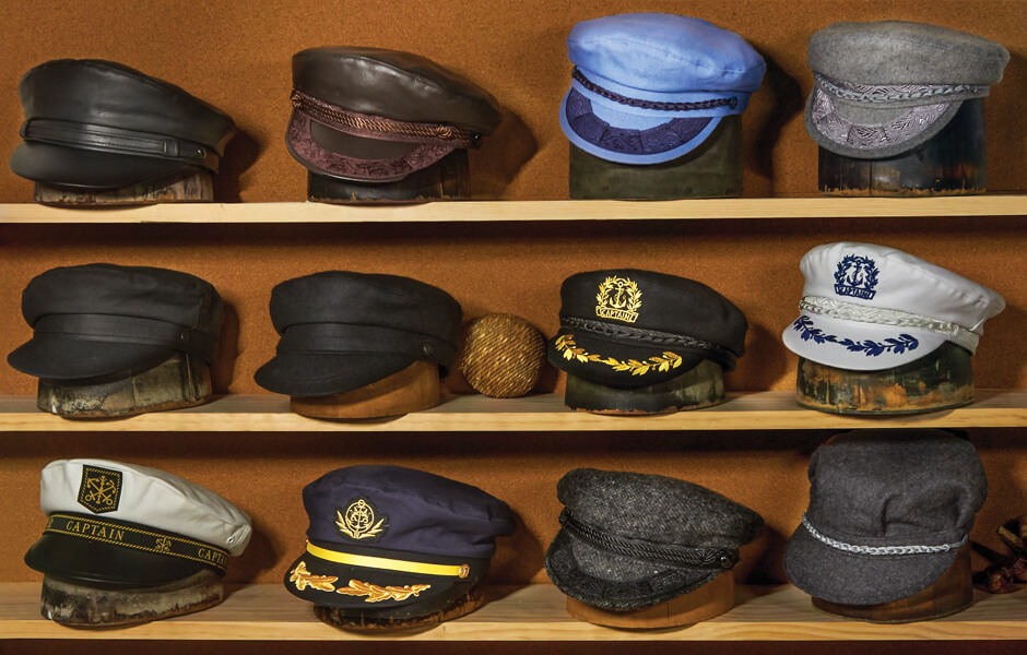 Three rows of Aegean hats displayed on hat blocks on a wooden shelf